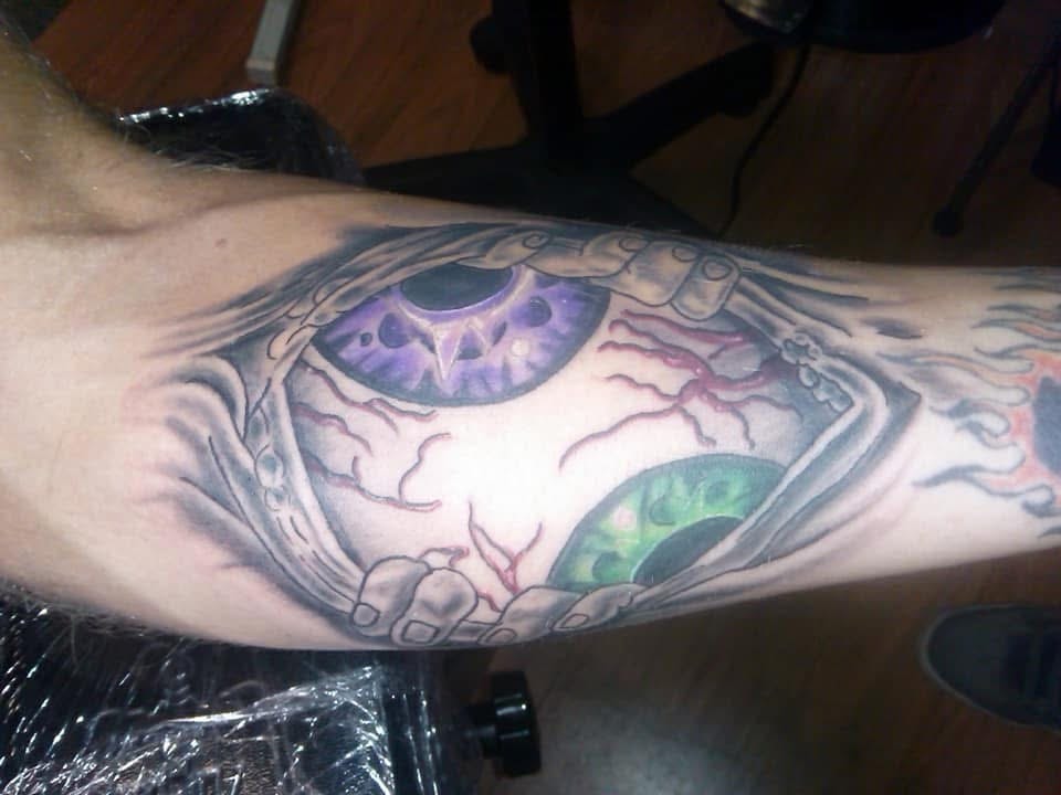 Skeleton hands holding eyeballs with purple and green irises forearm tattoo