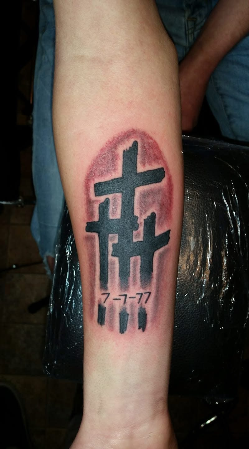 Three crosses with date 7-7-77 and red halo watercolor forearm tattoo