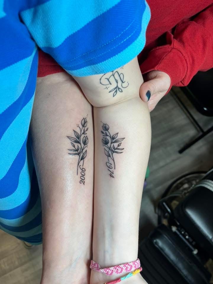 Matching fine line floral stems with birth year dates on forearms
