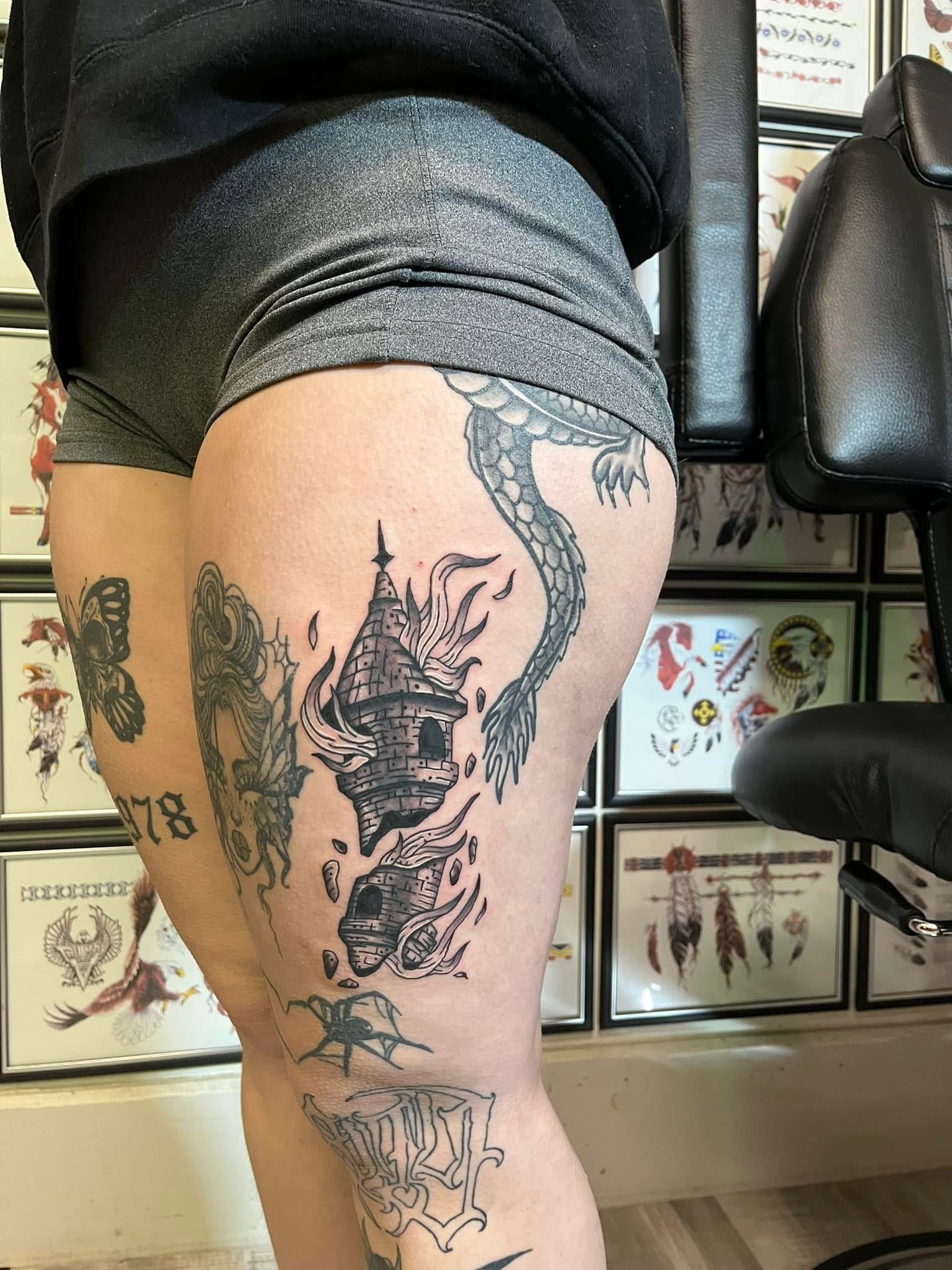 Dragon with burning castle tower thigh tattoo